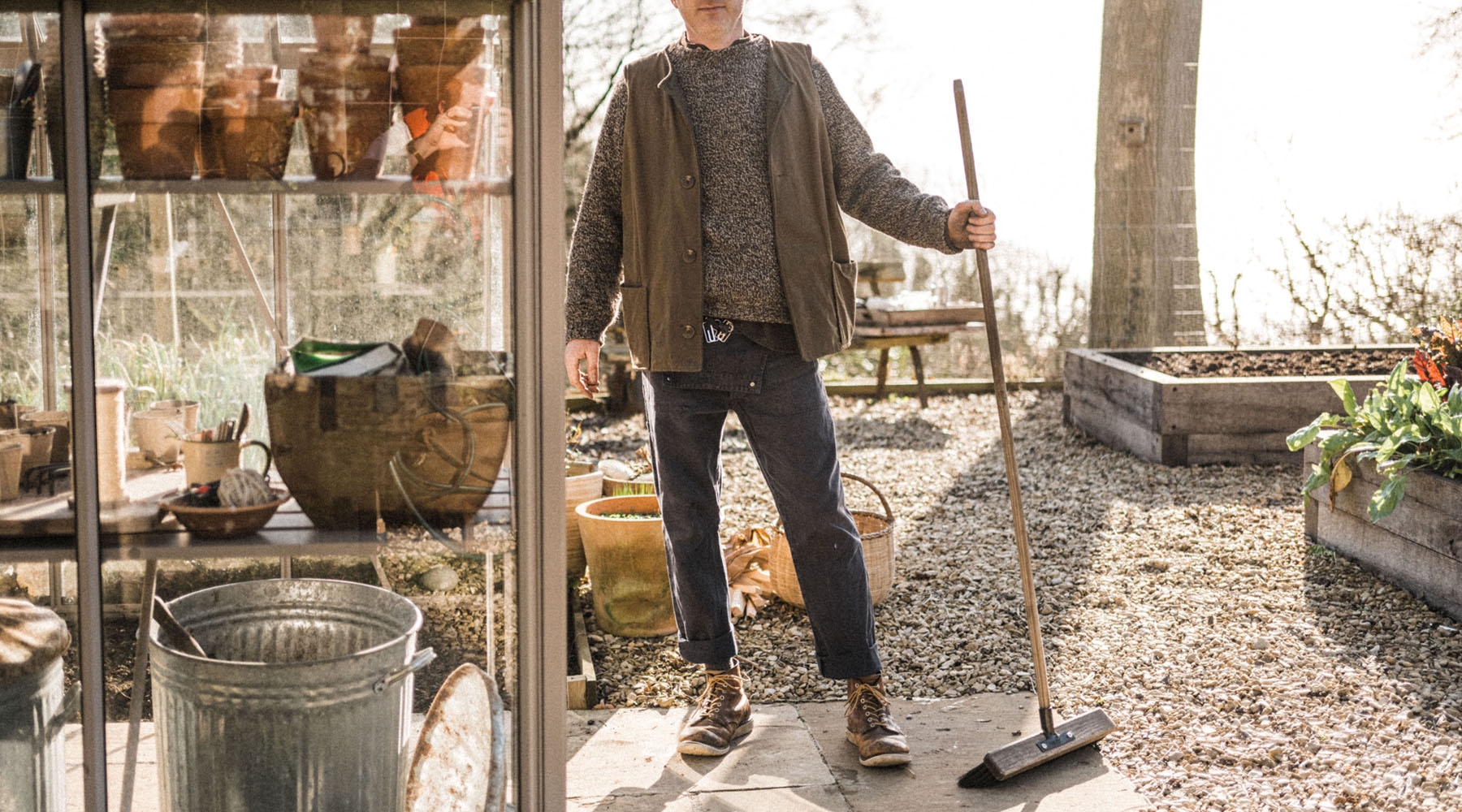 Man using a broom to sweep inside a greenhouse for greenhouse maintenance tasks